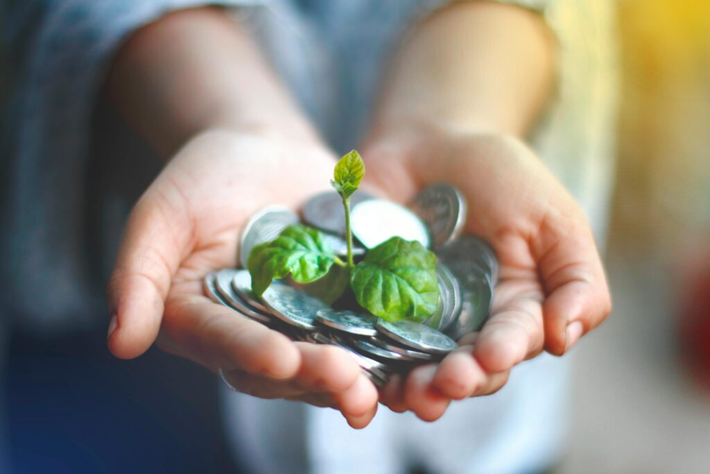Mãos segurando moedas com uma planta crescendo, simbolizando o fim do greenwashing e a transformação do ESG em estratégia corporativa com IFRS S1 e S2