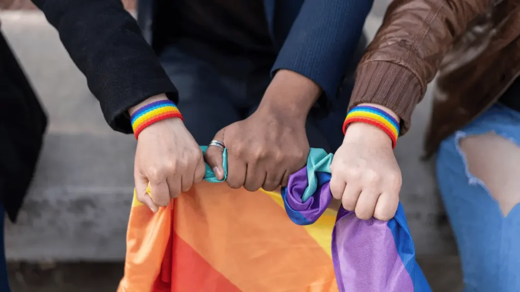 img lgbtfobia plurie 3 Três mãos segurando a bandeira do arco-íris